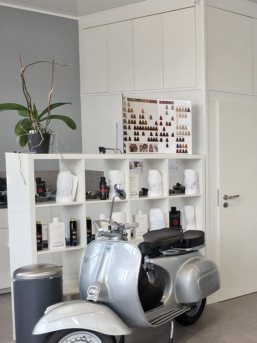 Regal mit Farbkarte und Produkten, davor die Vespa