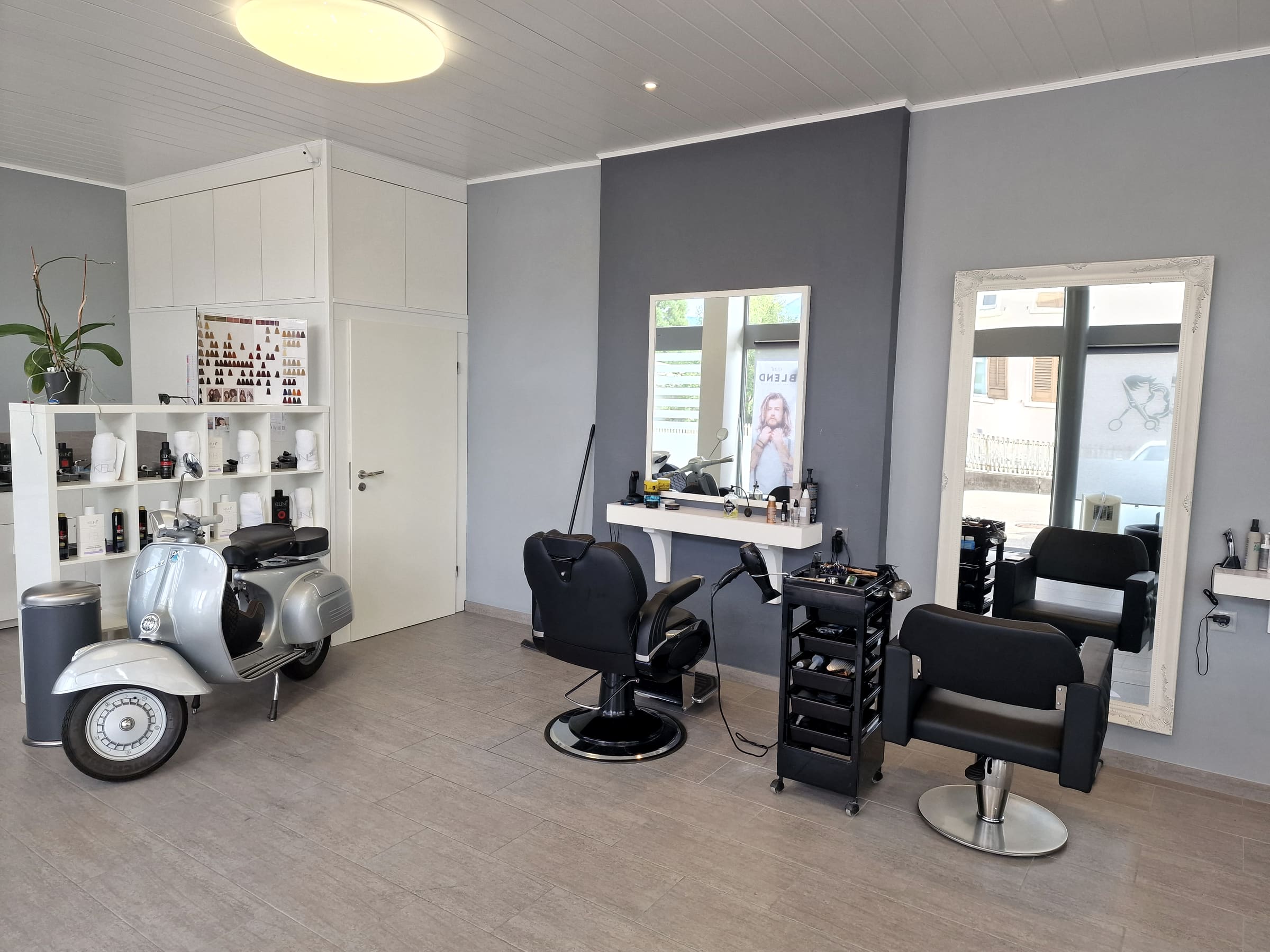 Blick in den Salon: zwei Arbeitsplätze mit weiss gerahmten Spiegeln, schwarze Stühle, die Vespa und ein Regal mit Produkten
