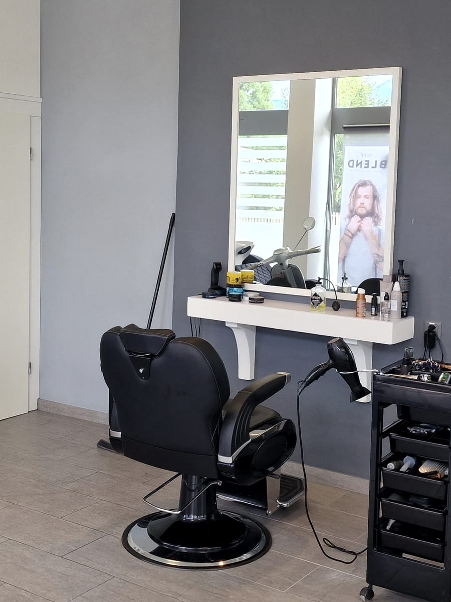 Schwarzer Barberstuhl vor einem Spiegel mit weissem Rahmen